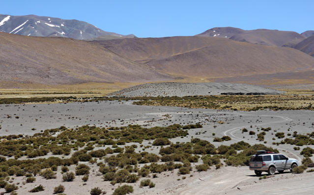 Tectoniq field vehicle on a gravel track across the high Altiplano, with snow-capped peaks behind