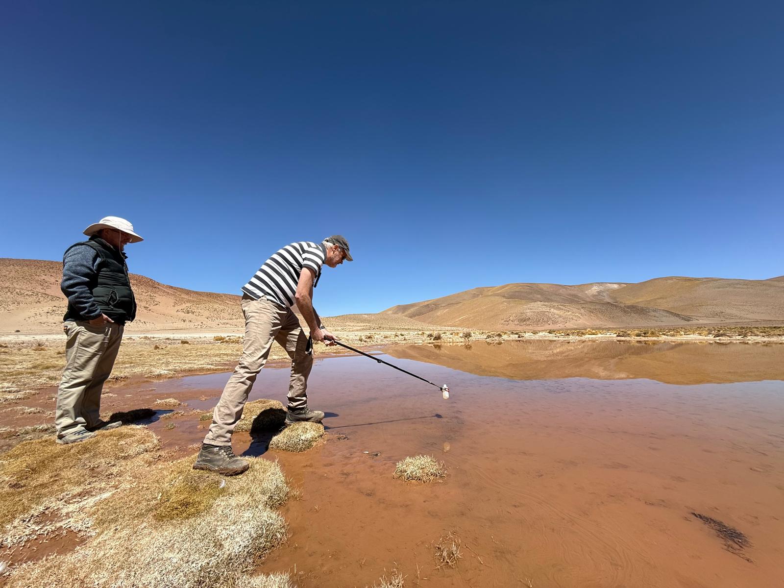 Tectoniq team collecting a water sample from a red, metal-rich spring pool on the Salta Altiplano